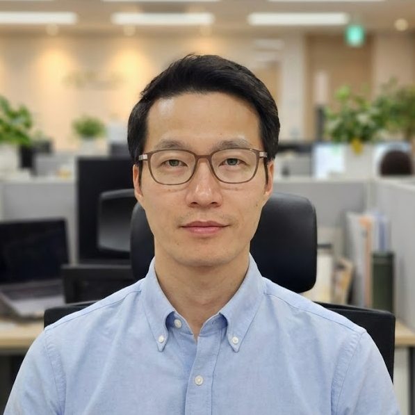 Professional headshot of Asian man with short black hair wearing dark blazer against neutral background
